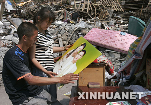 5月19日，雖然相框損壞了，夫妻倆還是仔細地把結婚照擦拭干凈。 四川省什邡市鎣華鎮仁和村三組的梁正彬一家很幸運，大地震發生時，包括老父母和年幼女兒在內的全家5口人都跑出了轟然倒塌的房屋。“平安就是福！”他們默默收拾廢墟中的家，準備重建家園。